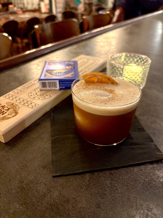 A Black Moon cribbage board on the bar beside a cocktail