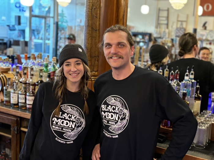 Two people behind the bar in black Black Moon long-sleeve shirts