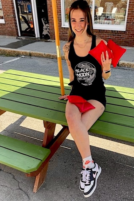 A woman in a black Black Moon tank top sitting on a picnic table