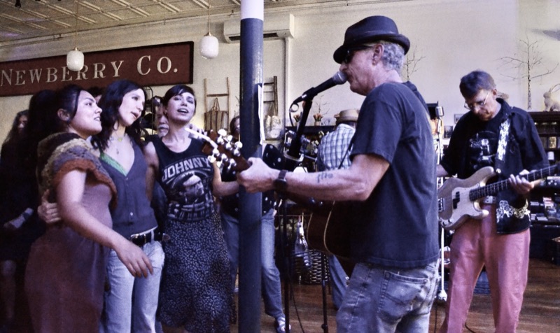 A band playing beneath the old Newberry Co. sign, a man with an acoustic guitar singing with three women