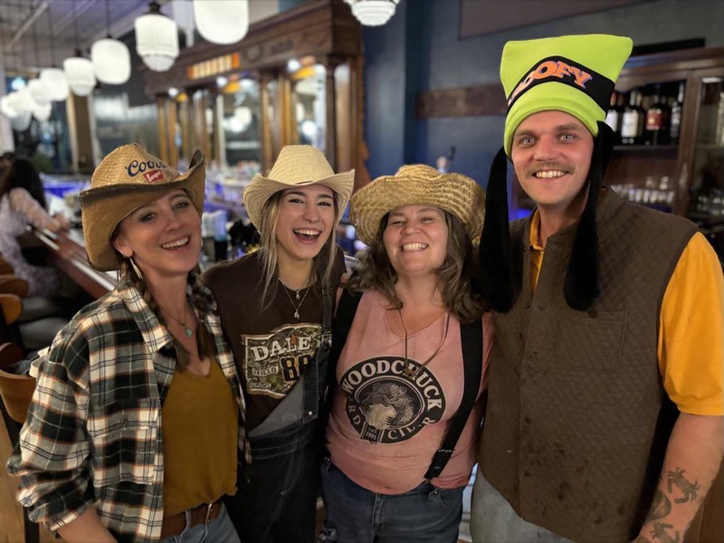 Four friends in cowboy hats and western wear smiling at the bar
