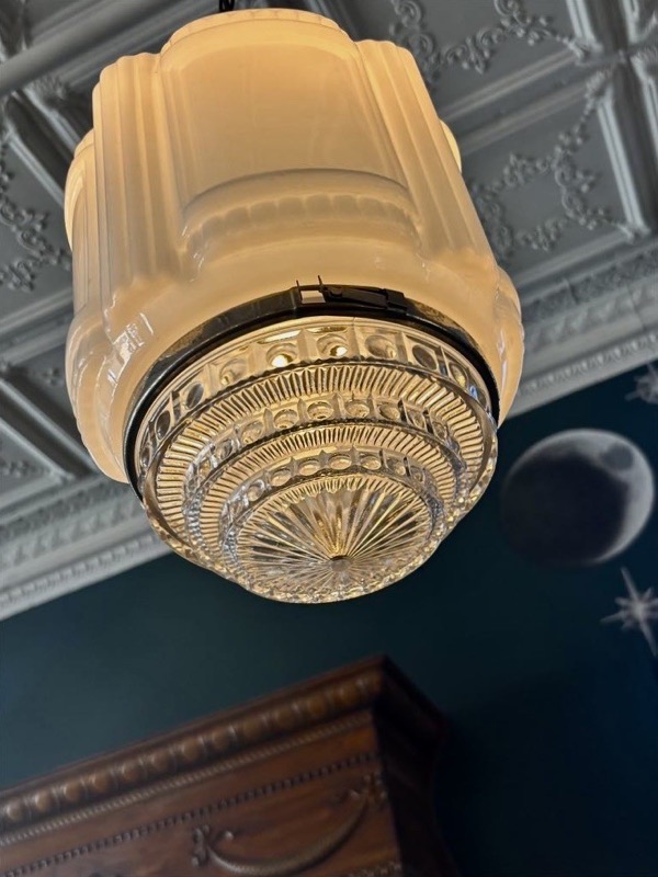 A milk-glass pendant light under the pressed tin ceiling, with a painted moon on the teal wall