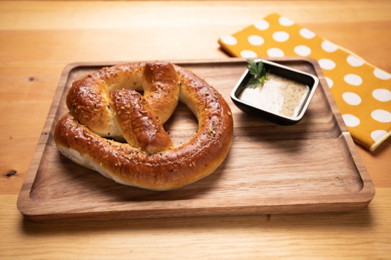 A soft pretzel with a cup of mustard on a wooden board